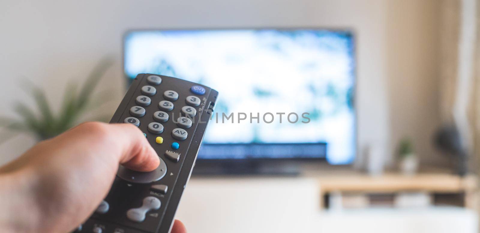 Male hand is holding TV remote control, streaming on a smart TV. by Daxenbichler