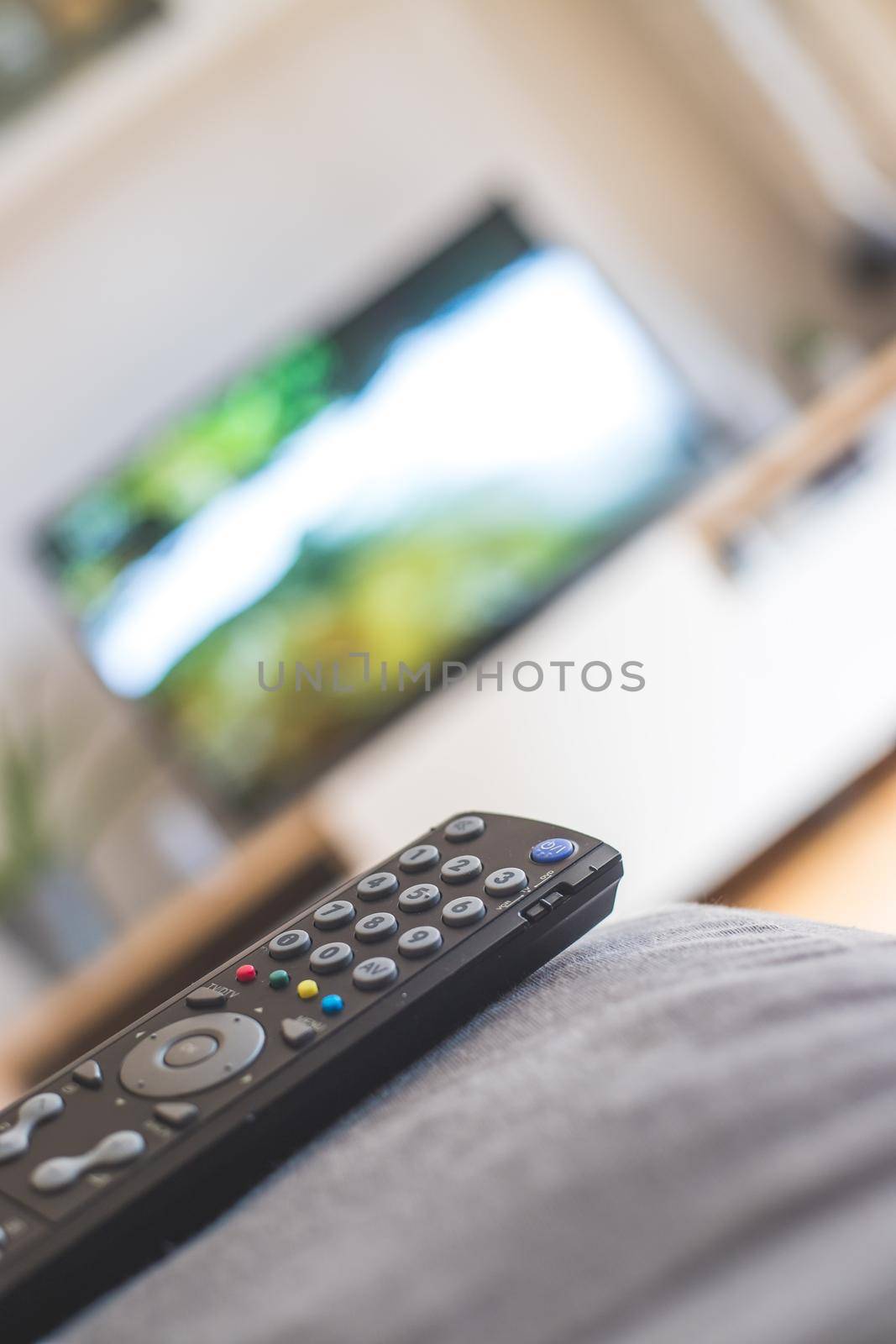 TV remote control in the foreground, tv in the blurry background. Streaming.