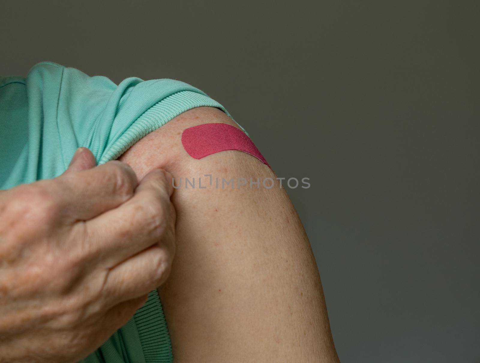 Senior caucasian man holding up shirt sleeve to show the bandaid after coronavirus vaccine shot in the shoulder