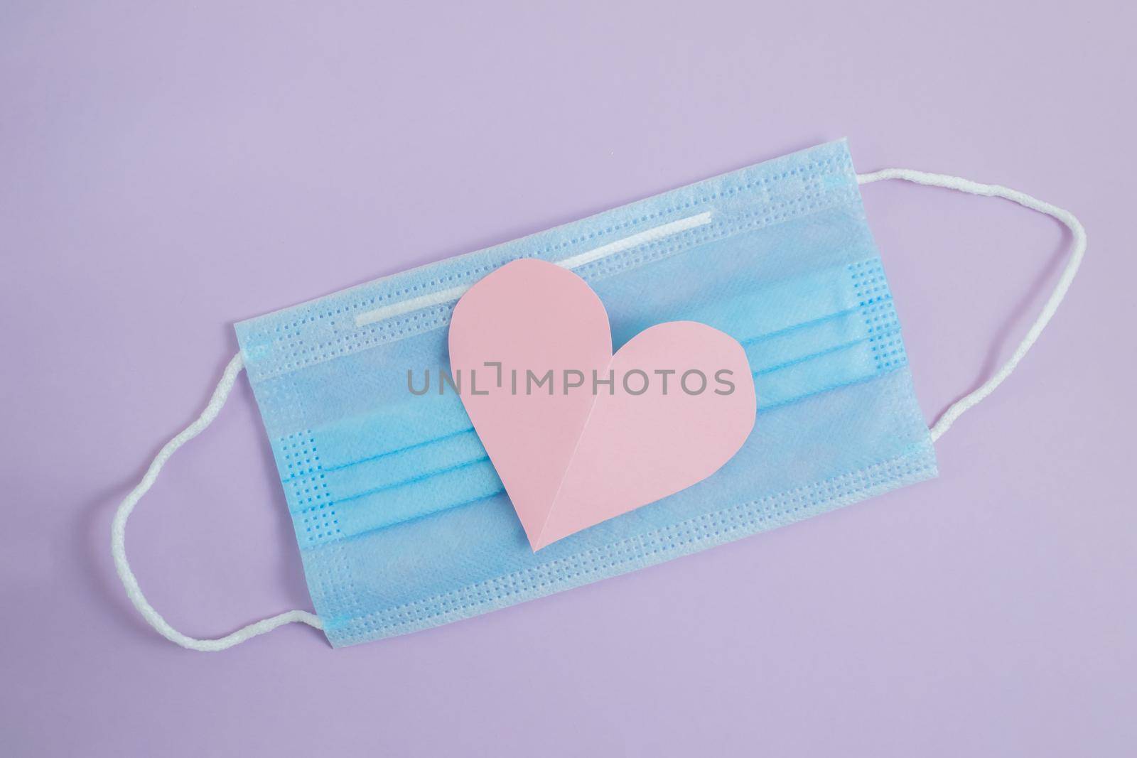 COVID-19. Face mask with cut paper heart on a purple background. Medical masks to protect against viruses and pollution. Concept of celebrating valentine's day in a new reality.