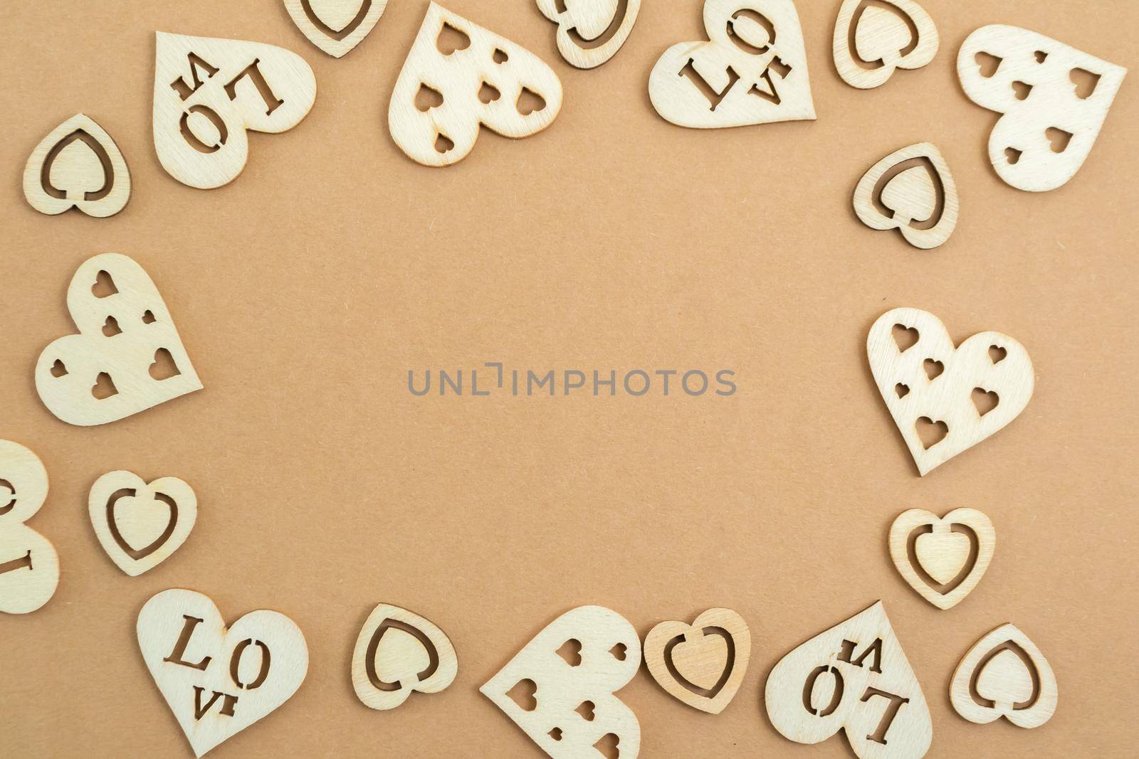 Wooden hearts on a pastel craft paper background in the form of a frame. Abstract background with wood cut shapes. Sainte Valentine. Copy space.