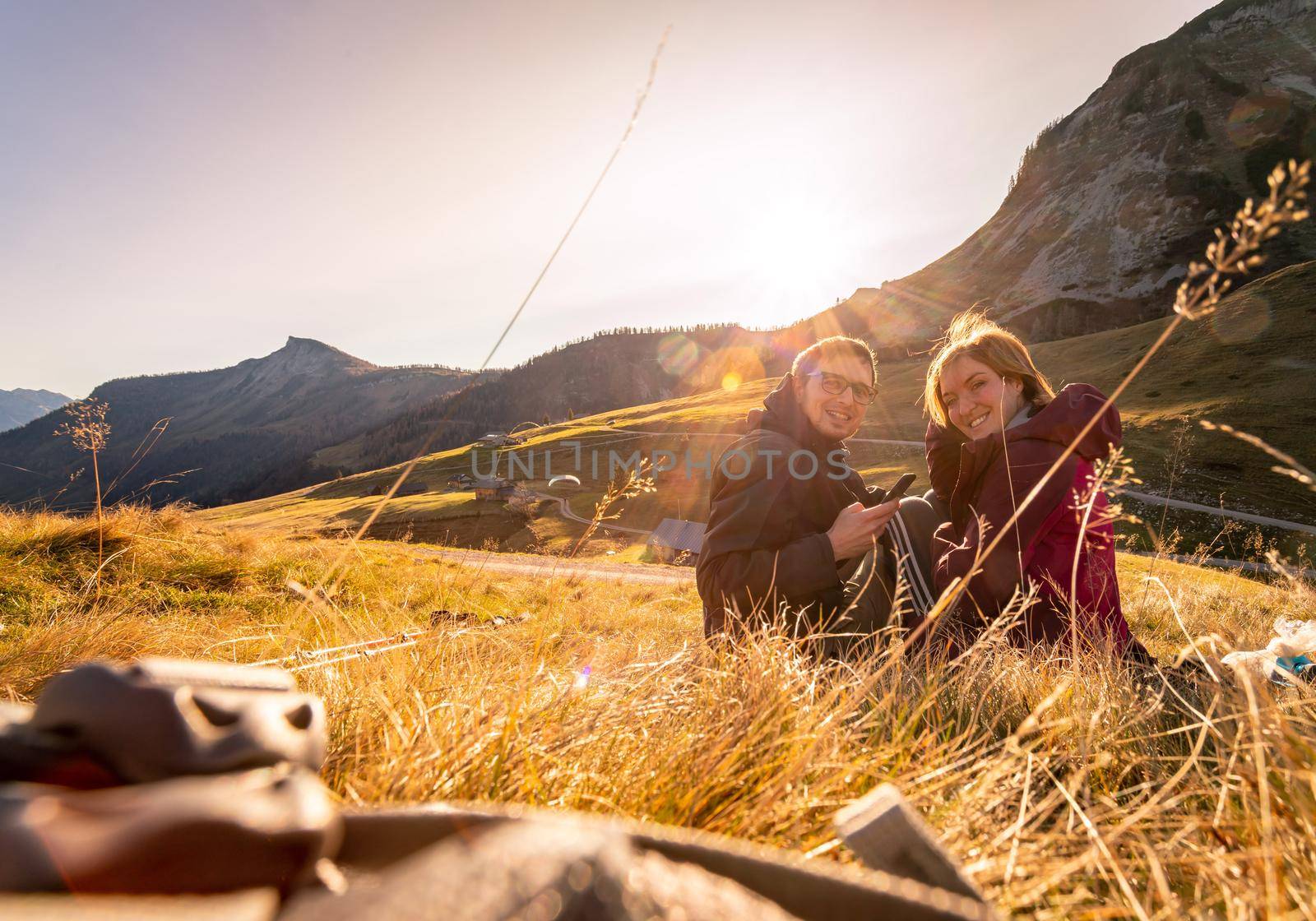 Loving couple is enjoying the sundown in the mountains, sitting on the ground. Warm colors, alps, Austria by Daxenbichler