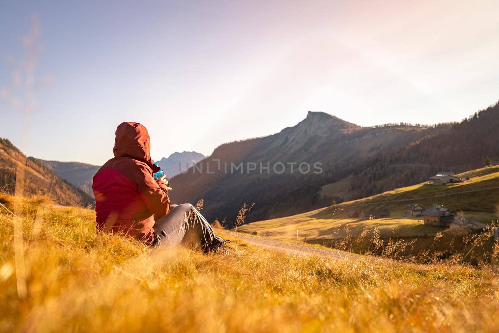 Hiking girl is enjoying the sundown in the mountains, sitting on the ground. Warm colors, alps, Austria by Daxenbichler