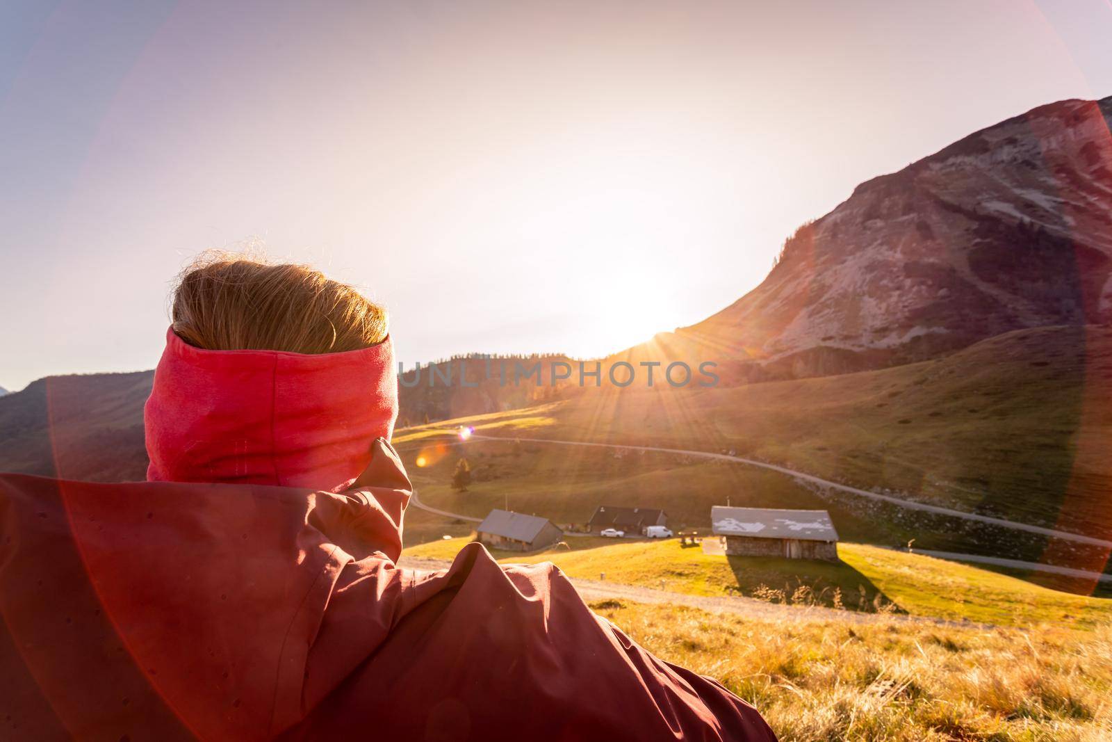 Hiking girl is enjoying the sundown in the mountains, sitting on the ground. Warm colors, alps, Austria by Daxenbichler