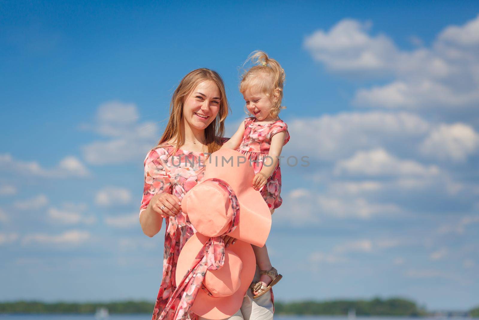 A charming girl in a light summer sundress walks on the sandy beach with her little daughter. Enjoys warm sunny summer days. by Try_my_best