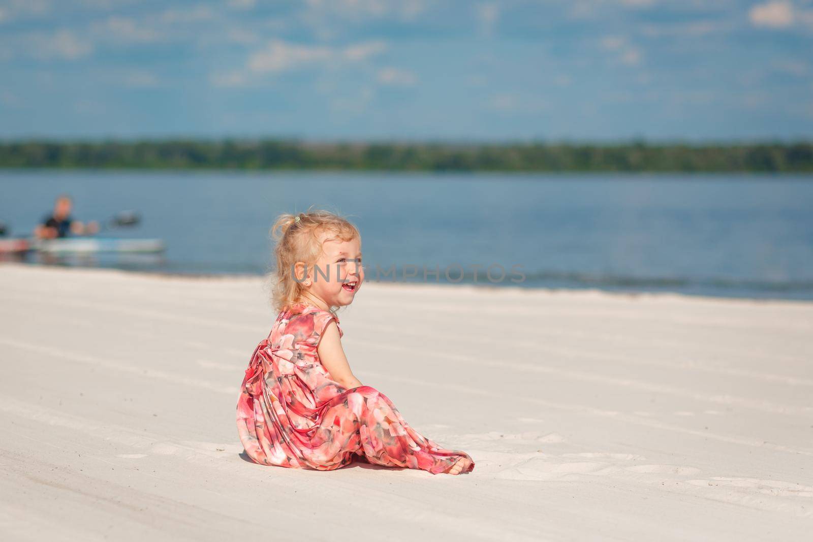 A little girl in a beautiful sarafna plays in the sand on the beach.