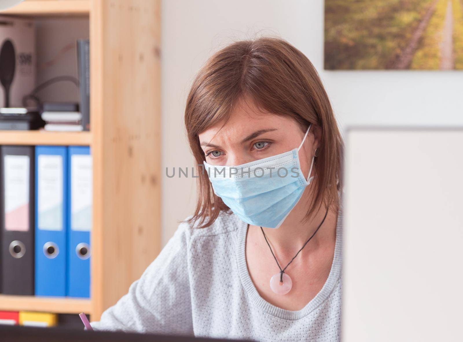 Protection in office in corona crisis: Woman with face mask is sitting on his workplace by Daxenbichler