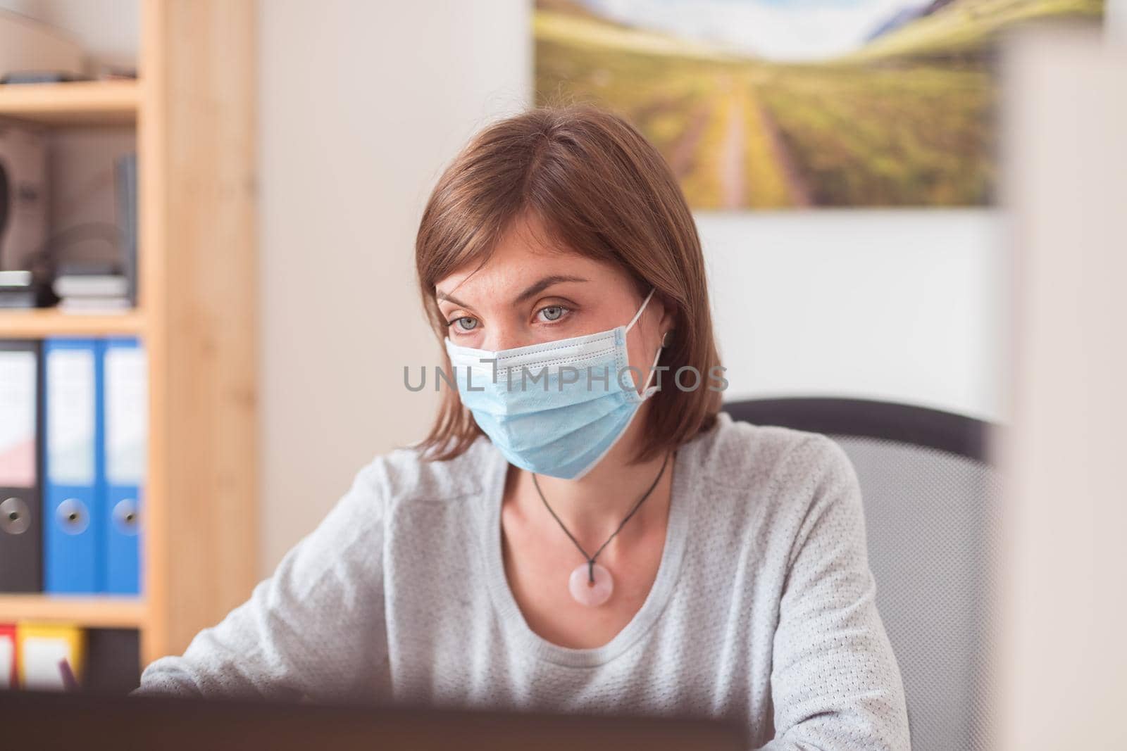 Protection in office in corona crisis: Woman with face mask is sitting on his workplace by Daxenbichler