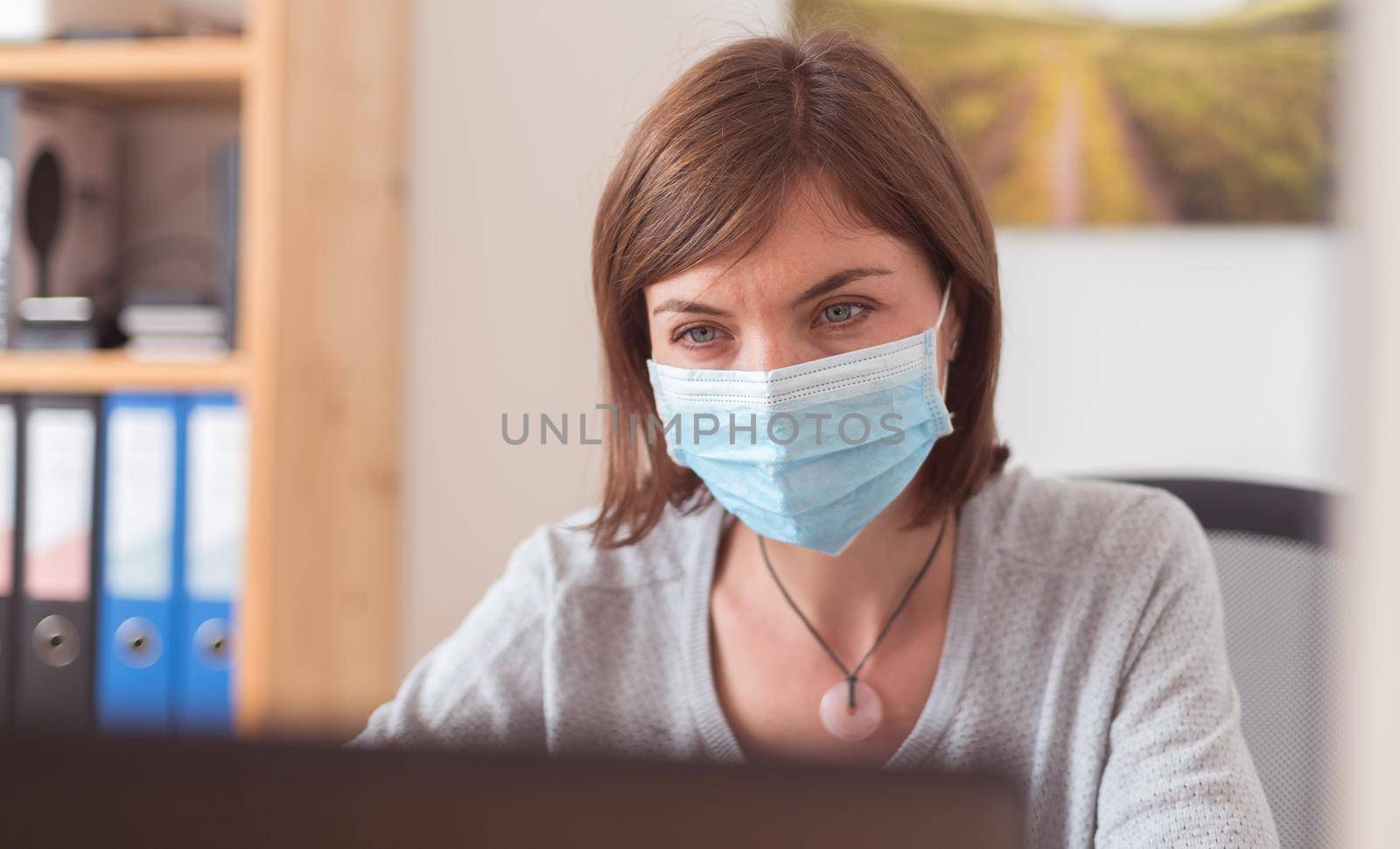 Protection in office in corona crisis: Woman with face mask is sitting on his workplace by Daxenbichler