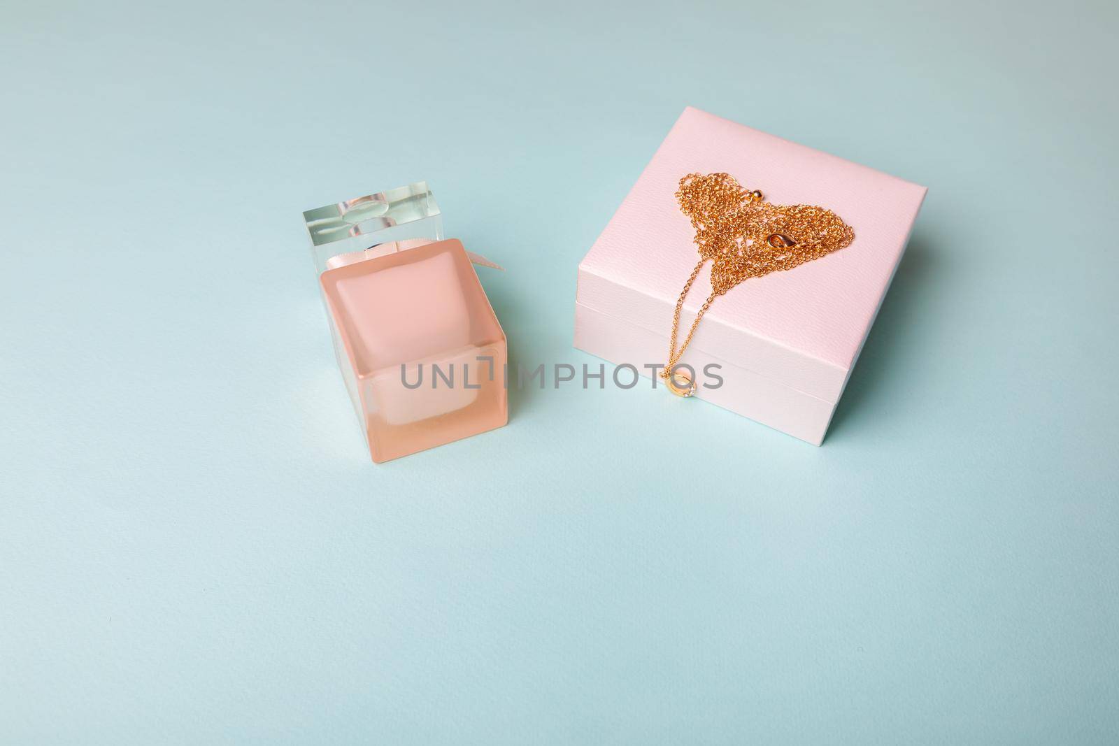 A gift for Valentine's Day. Perfume and a box with a gold chain on a blue background. Chain in the shape of a heart.