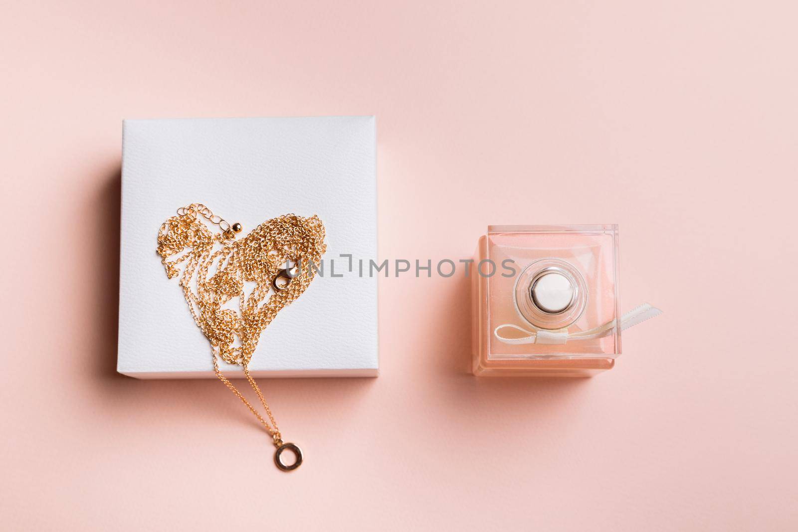 A gift for Valentine's Day. Perfume and a box with a gold chain on a pink background.
