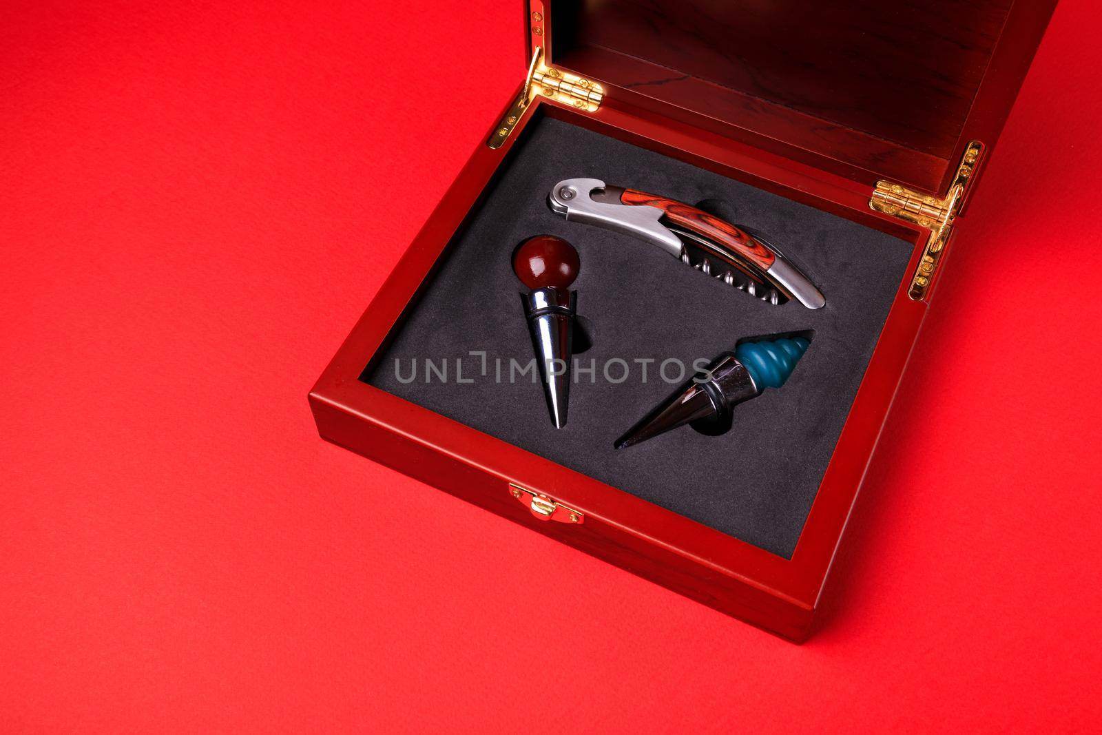 Gift set of corkscrew and removable lids. Wine corks and bottle openers in a wooden box on a red background.