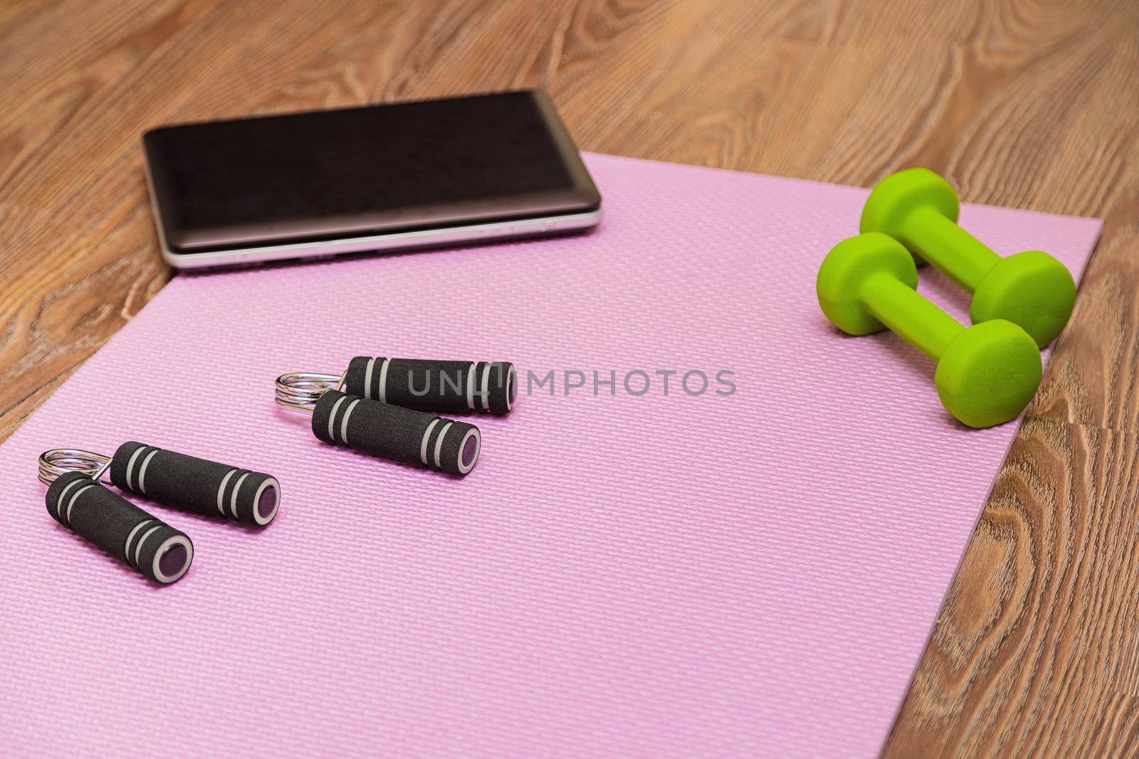 Fitness mat, dumbbells, expander and laptop for online workouts at home. Online learning concept in relation to the pandemic