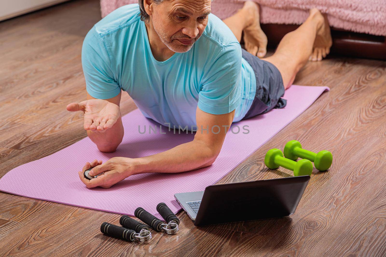 50 year old man performs exercises lying on mat at home looking at computer by Yurich32