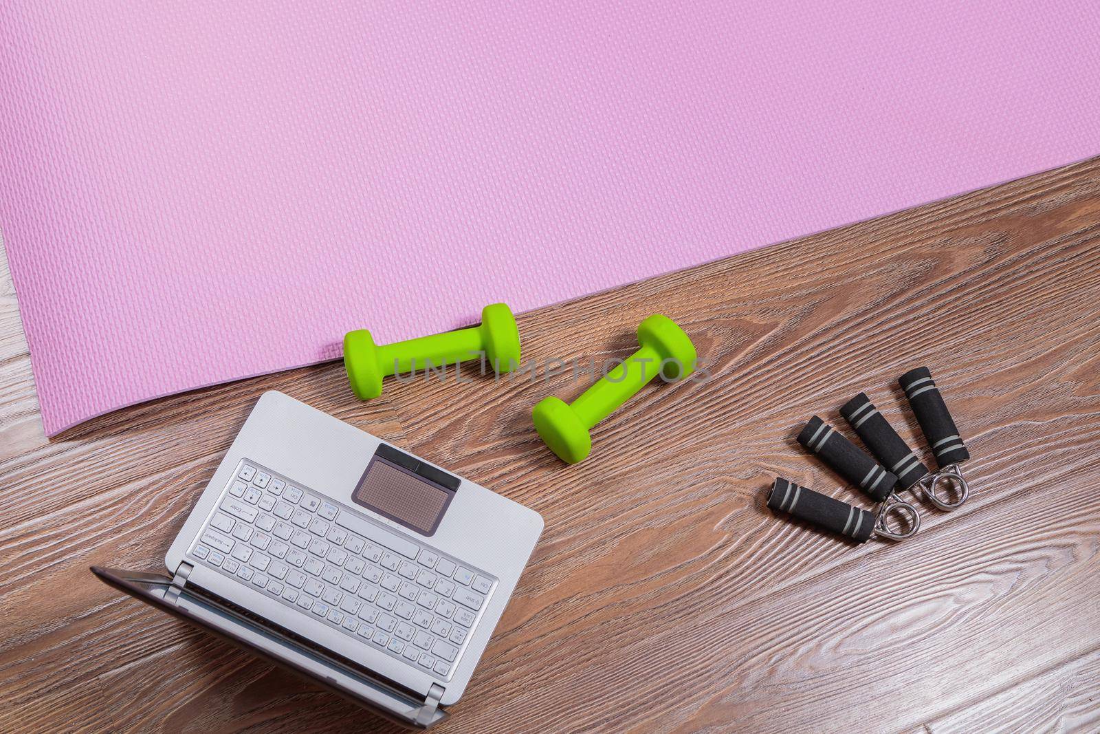 Fitness mat, dumbbells, expander and laptop for online workouts at home. Online learning concept in relation to the pandemic