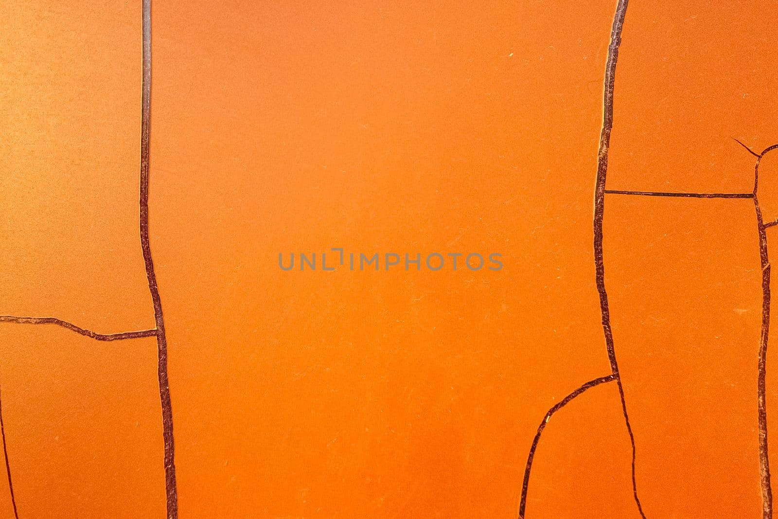 Cracked orange paint on the wall. The texture has peeled off under the influence of atmospheric influences. Background with large cracks.