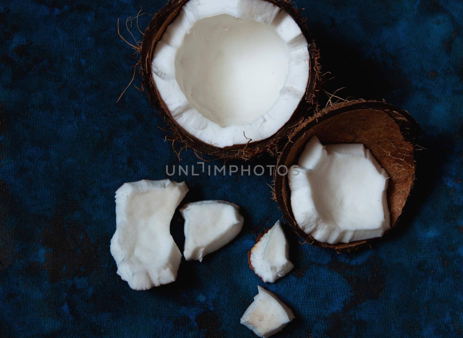 Open coconut lies on a dark blue background next to broken pieces lying randomly by ozornina