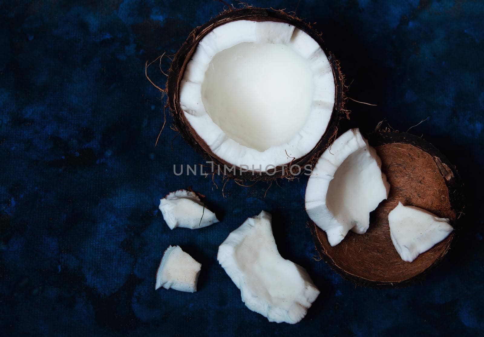 Open coconut lies on a dark blue background next to broken pieces lying randomly by ozornina