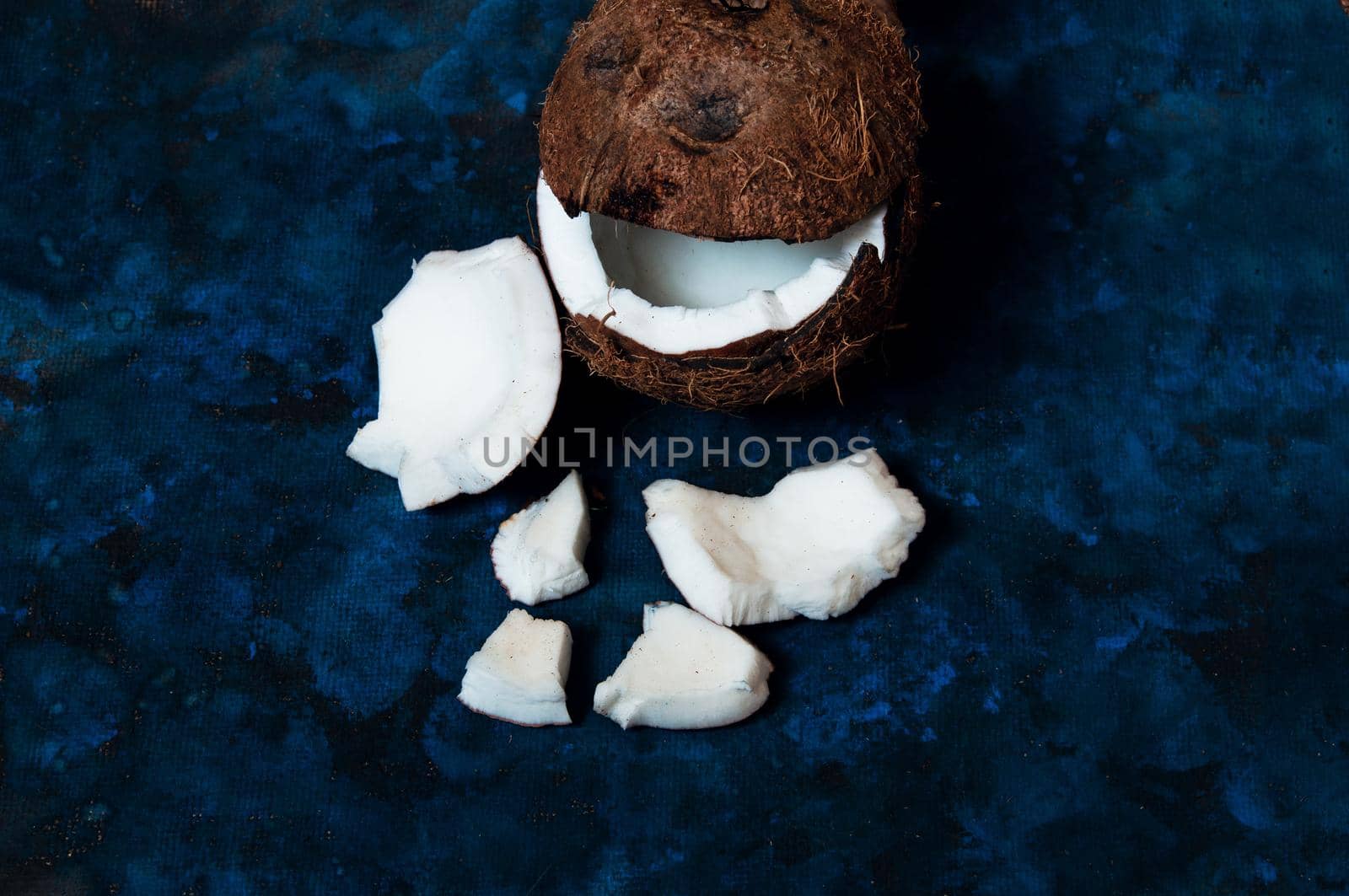 Open coconut lies on a dark blue background next to broken pieces lying randomly