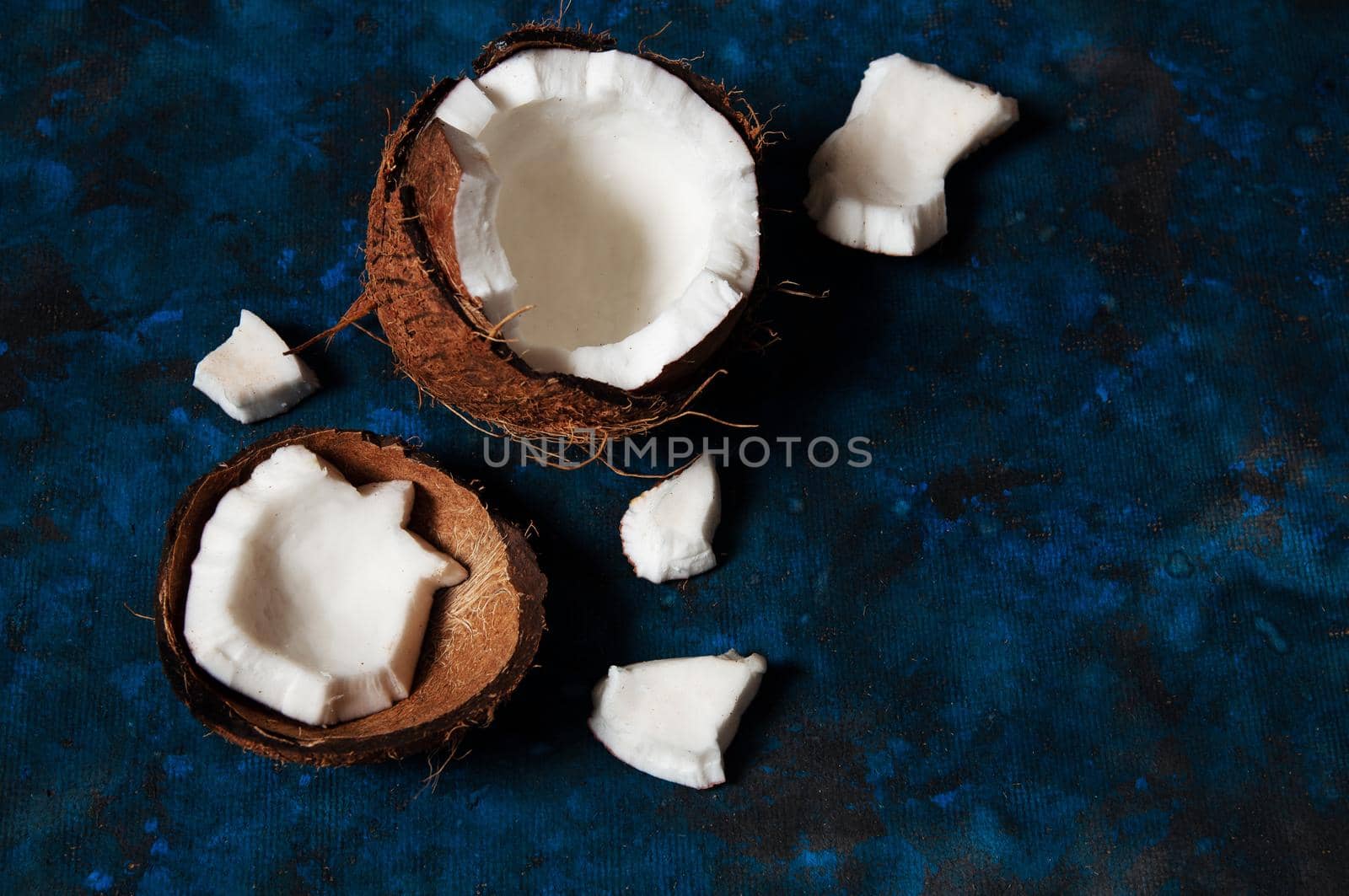 Open coconut lies on a dark blue background next to broken pieces lying randomly