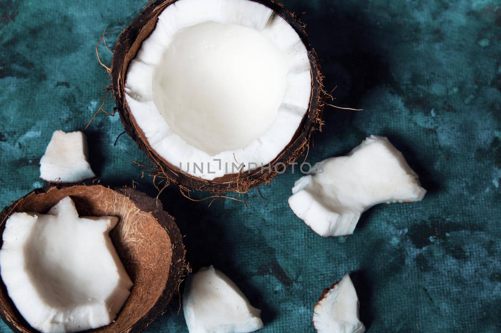 Open coconut lies on a dark blue background next to broken pieces lying randomly