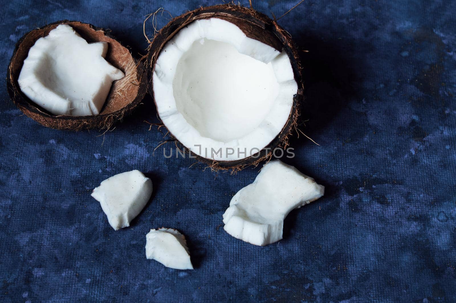 Open coconut lies on a dark blue background next to broken pieces lying randomly