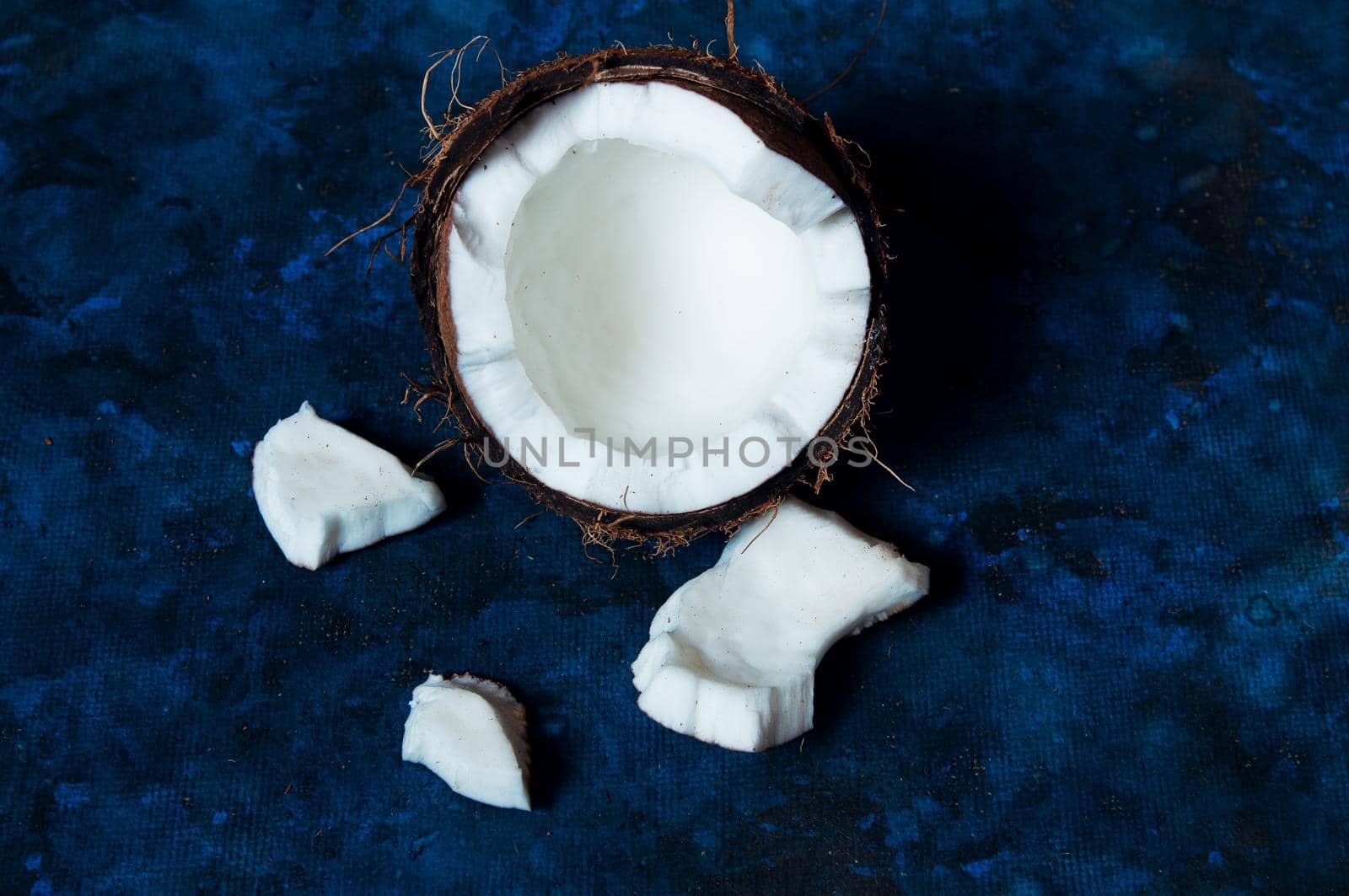 Open coconut lies on a dark blue background next to broken pieces lying randomly