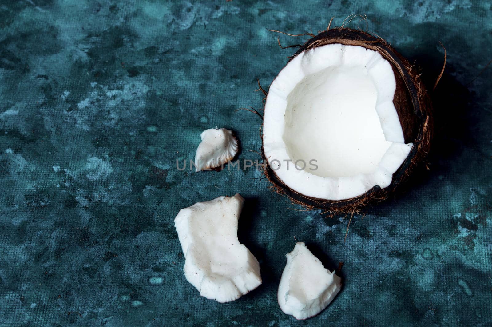 Open coconut lies on a dark blue background next to broken pieces lying randomly