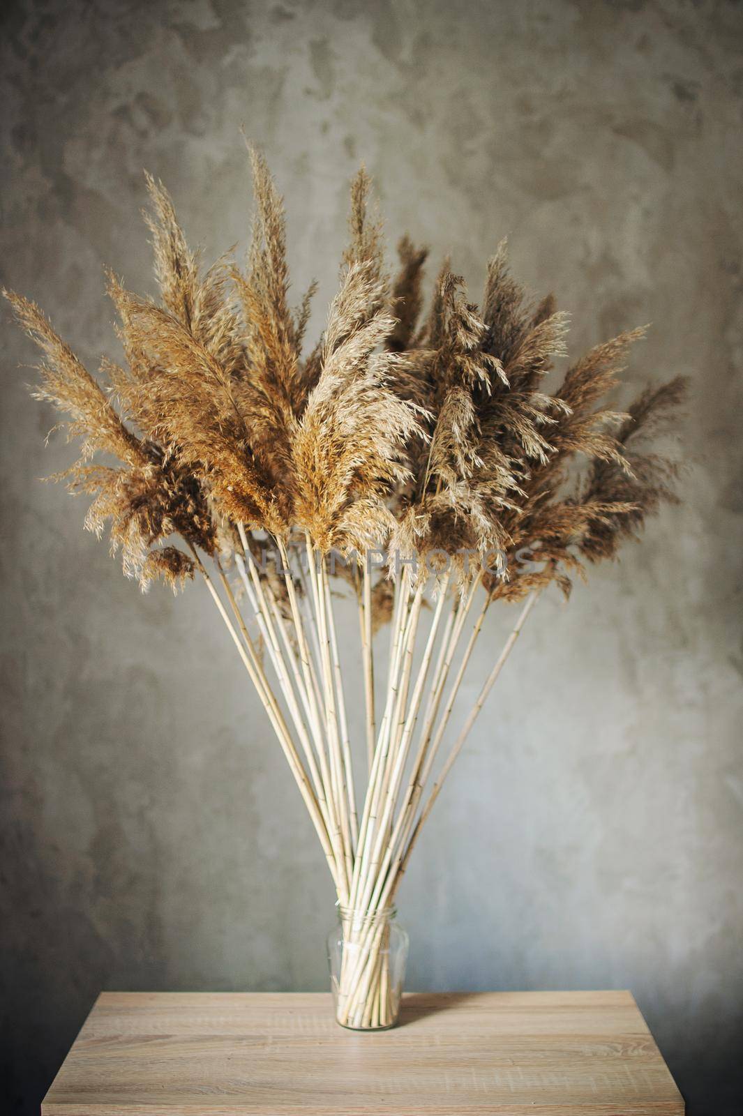 bouquet of dried flowers in brown tones stands on a wooden table in a room near a concrete wall in a loft style