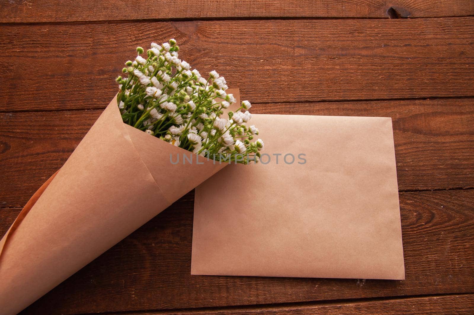 envelope made of craft paper, next to a bouquet of chamomile flowers, which lies on a wooden table