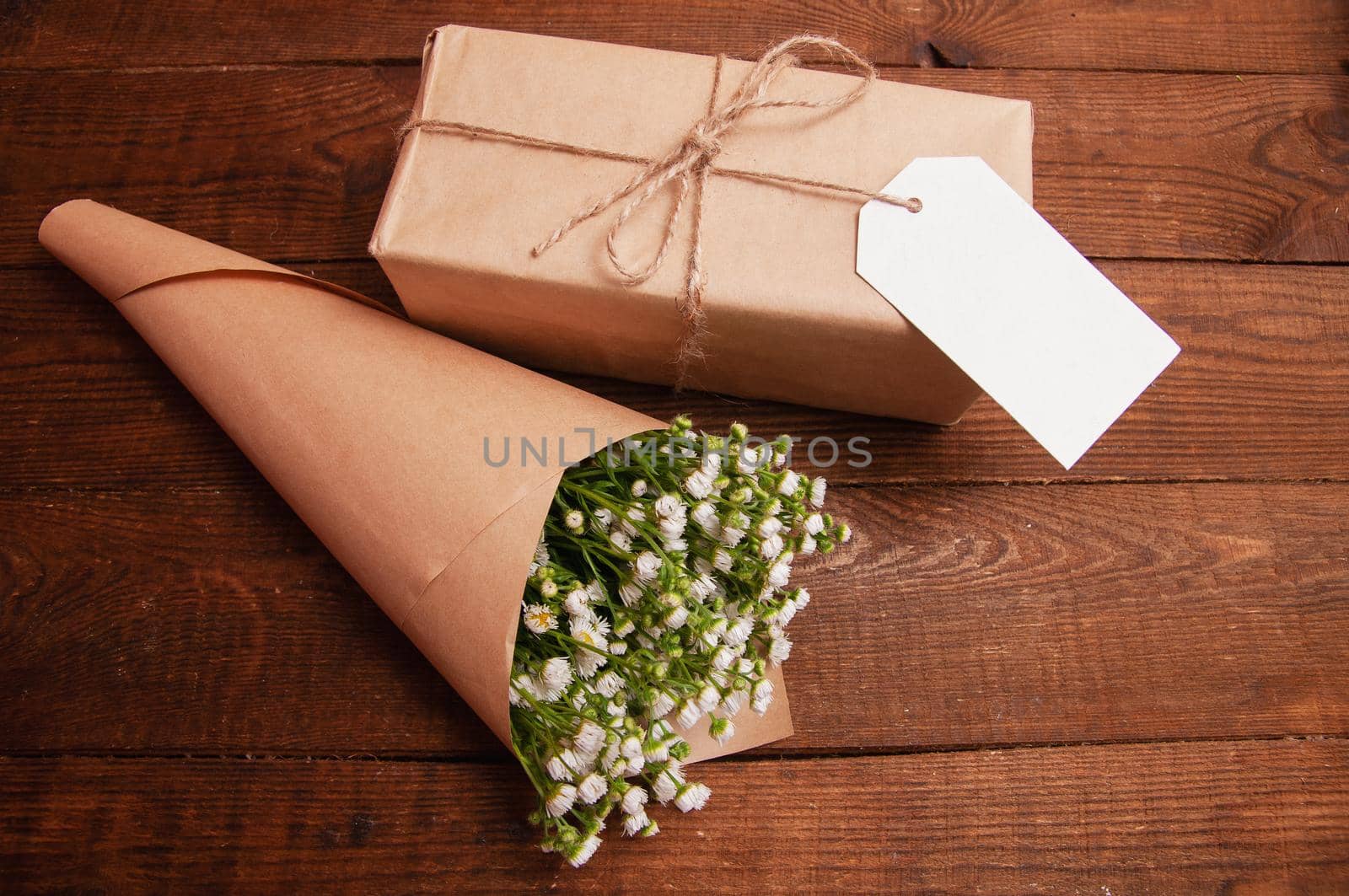 gift is wrapped in craft paper, next to it is a bouquet of chamomile flowers  by ozornina