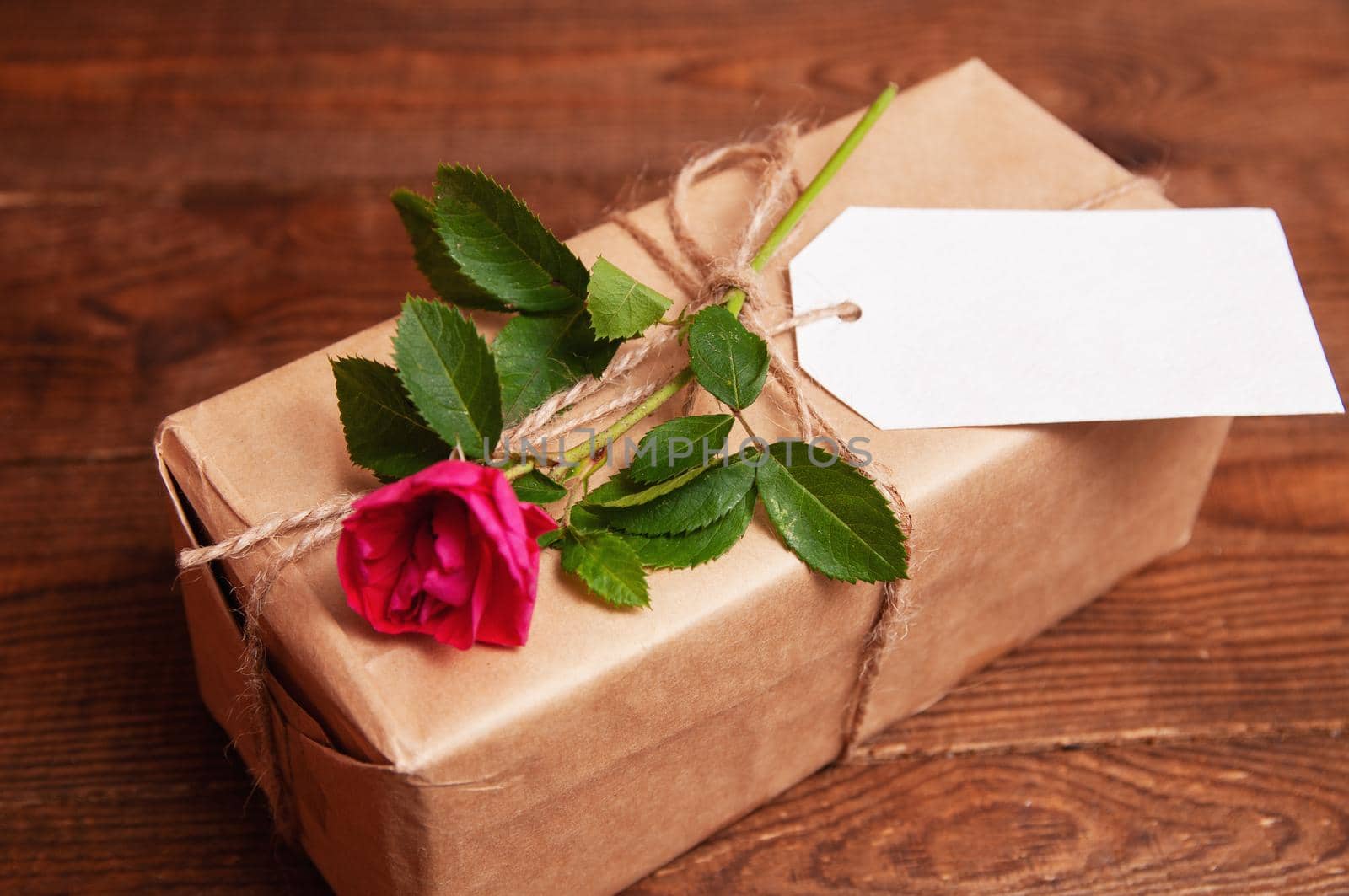 gift wrapped in craft paper on top of a flower rose tied with twine, which lies on a wooden table