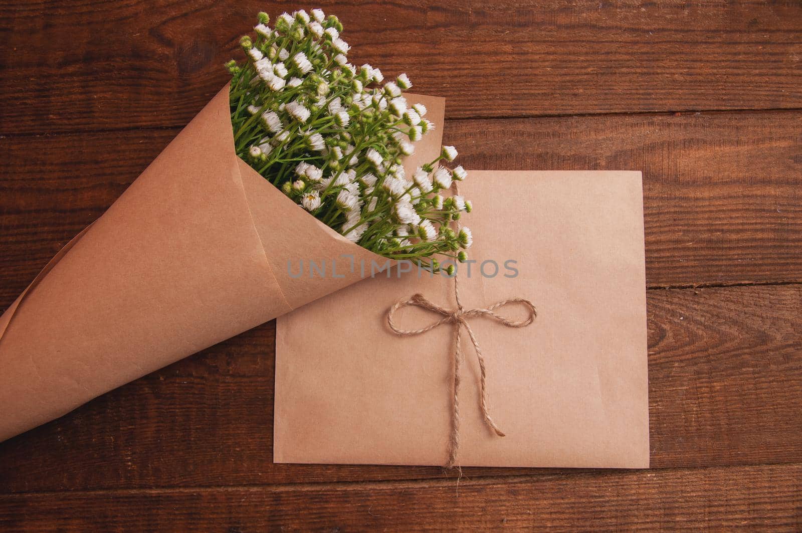 envelope made of craft paper, next to a bouquet of chamomile flowers, which lies on a wooden table