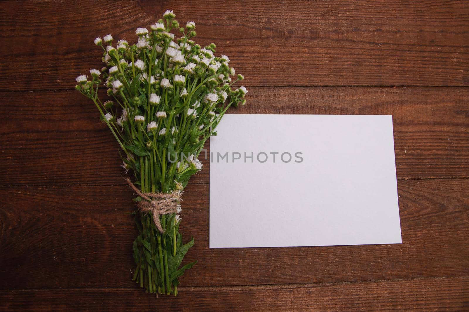 envelope made of craft paper, next to a bouquet of chamomile flowers, which lies on a wooden table