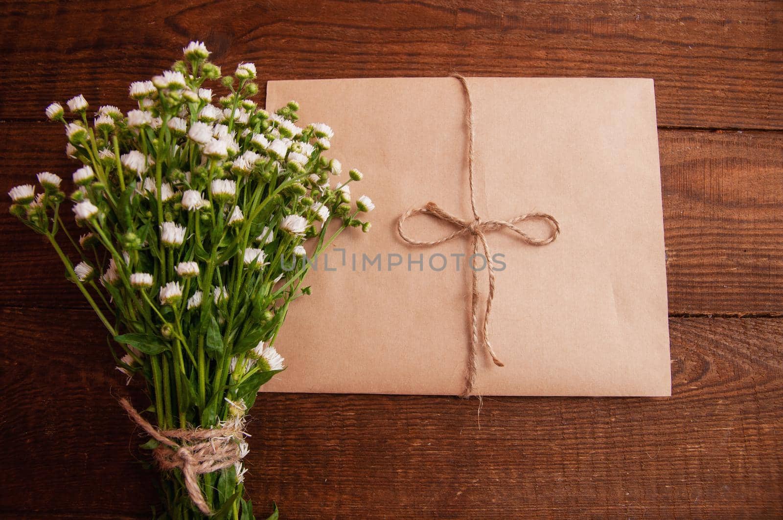 envelope made of craft paper, next to a bouquet of chamomile flowers, which lies on a wooden table