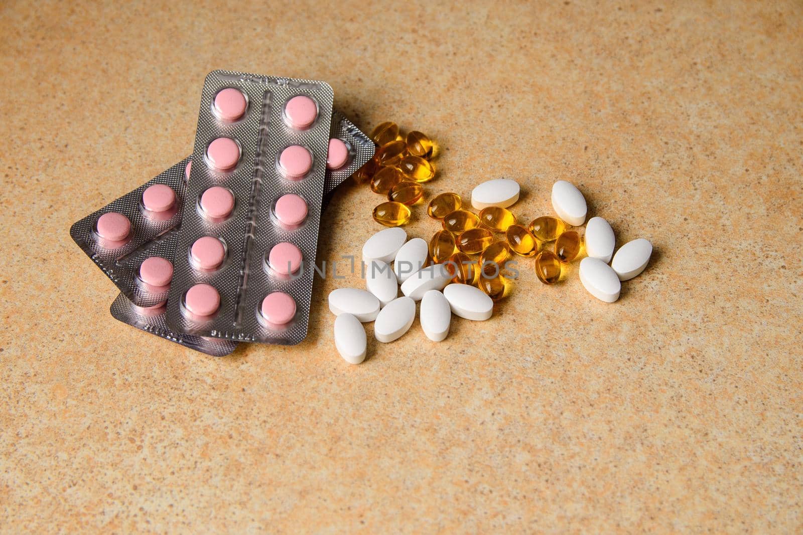 amber, pink and white capsules on a table with a pattern of sand