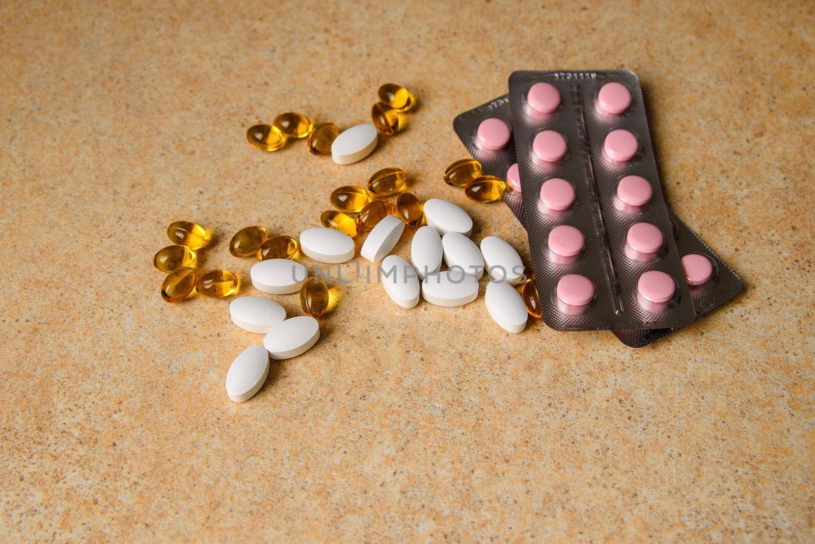 amber, pink and white capsules on a table with a pattern of sand