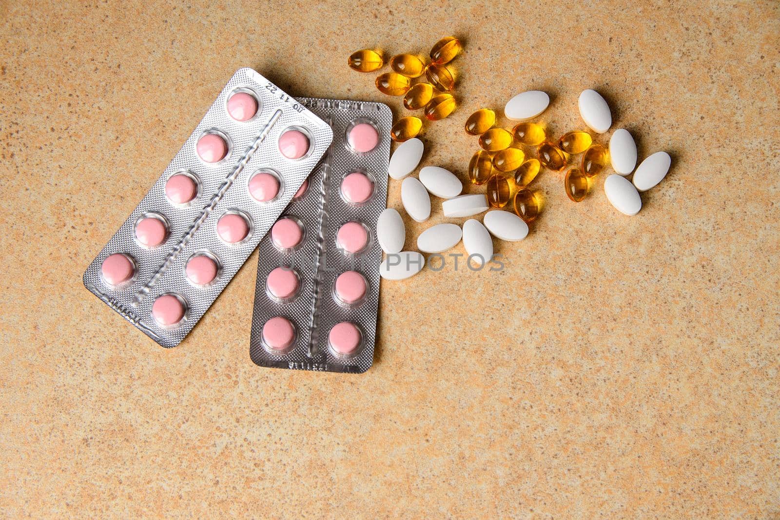 amber, pink and white capsules on a table with a pattern of sand