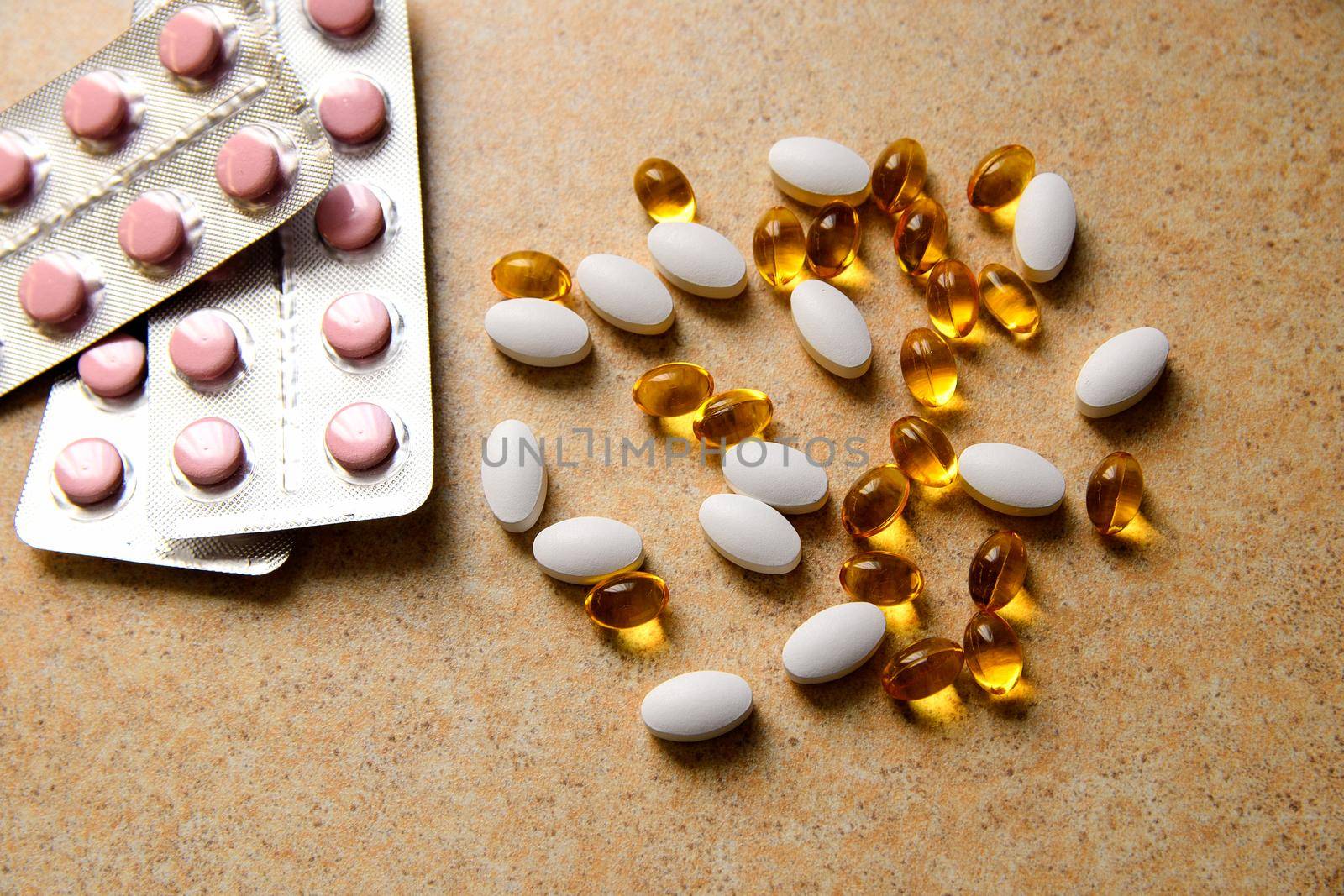 blister with pink tablets and vitamin D and capsules with fish oil lie chaotically against the background of a sand countertop