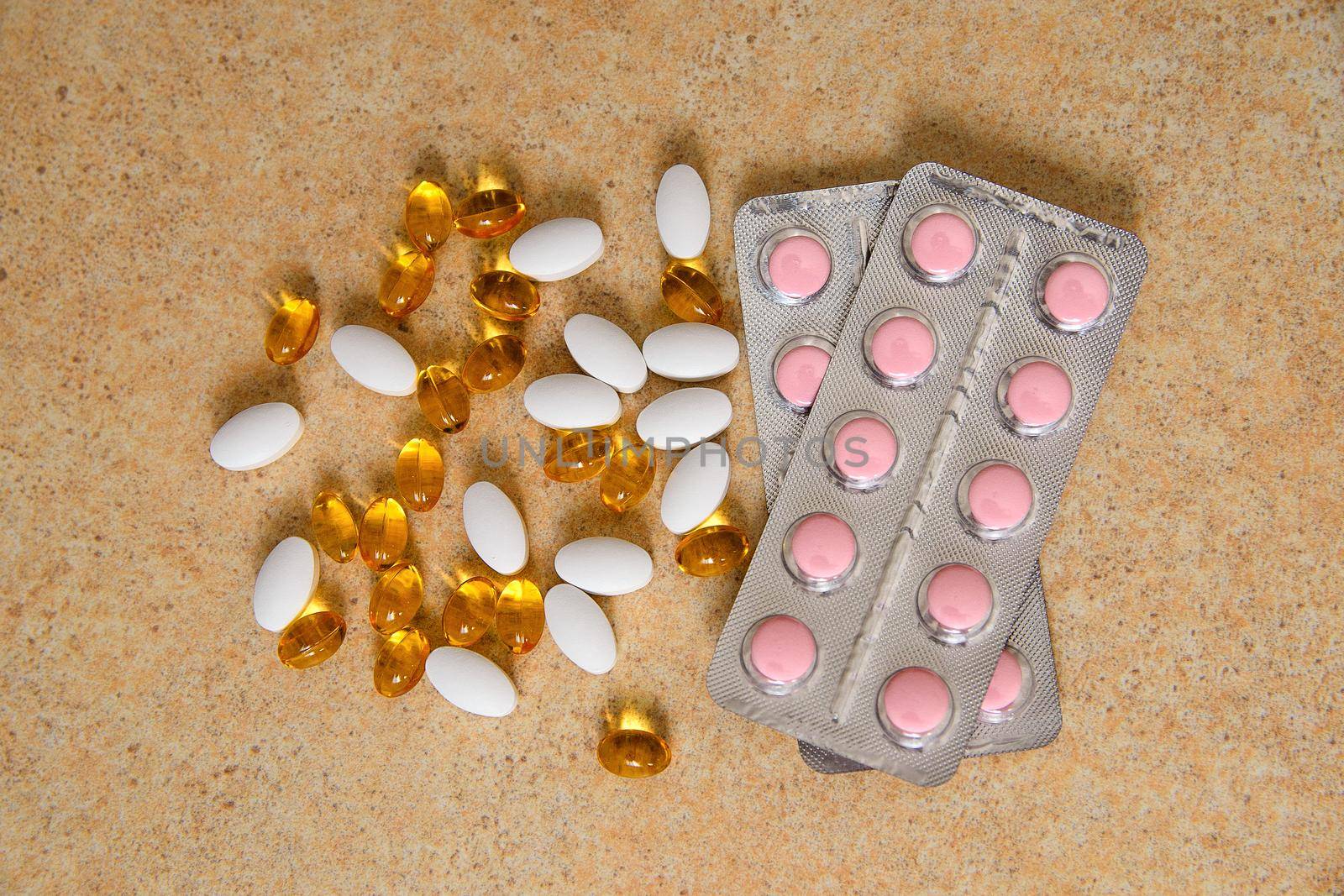 blister with pink tablets and vitamin D and capsules with fish oil lie chaotically against the background of a sand countertop