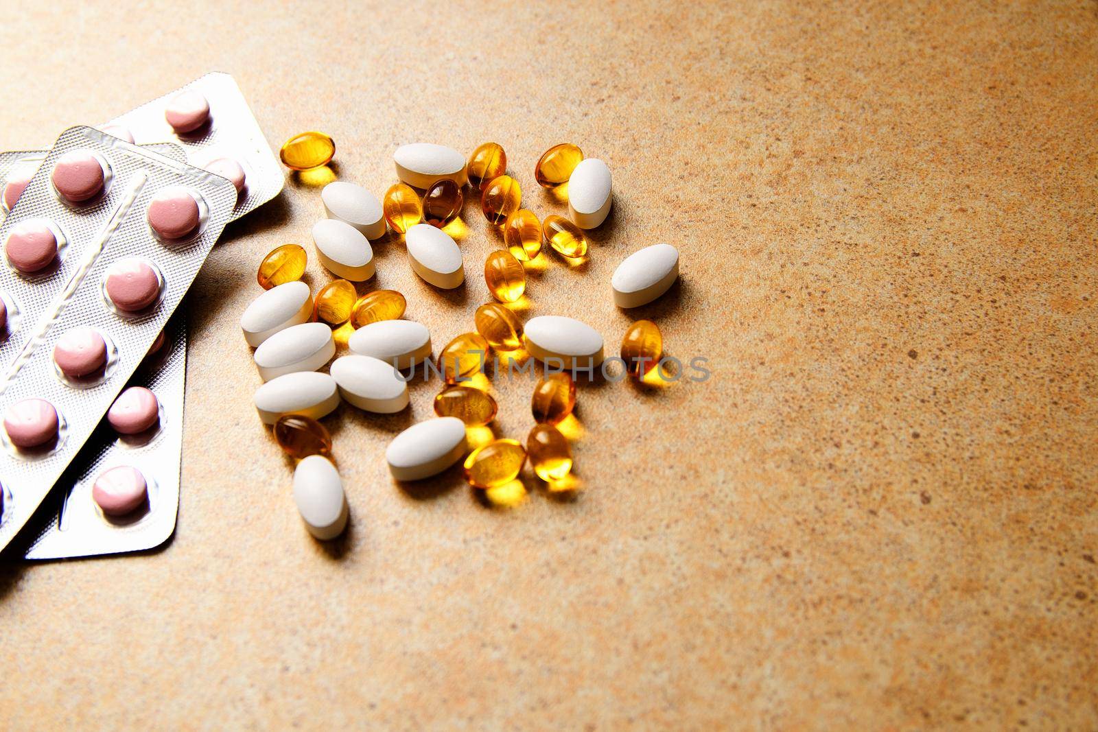 blister with pink tablets and vitamin D and capsules with fish oil lie chaotically against the background of a sand countertop