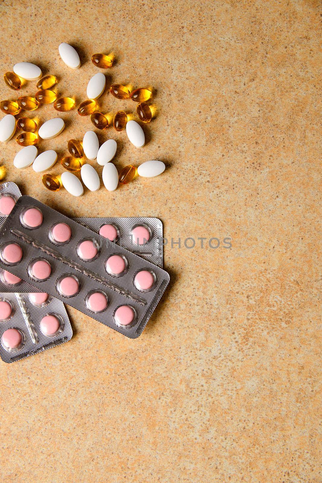 blister with pink tablets and vitamin D and capsules with fish oil lie chaotically against the background of a sand countertop