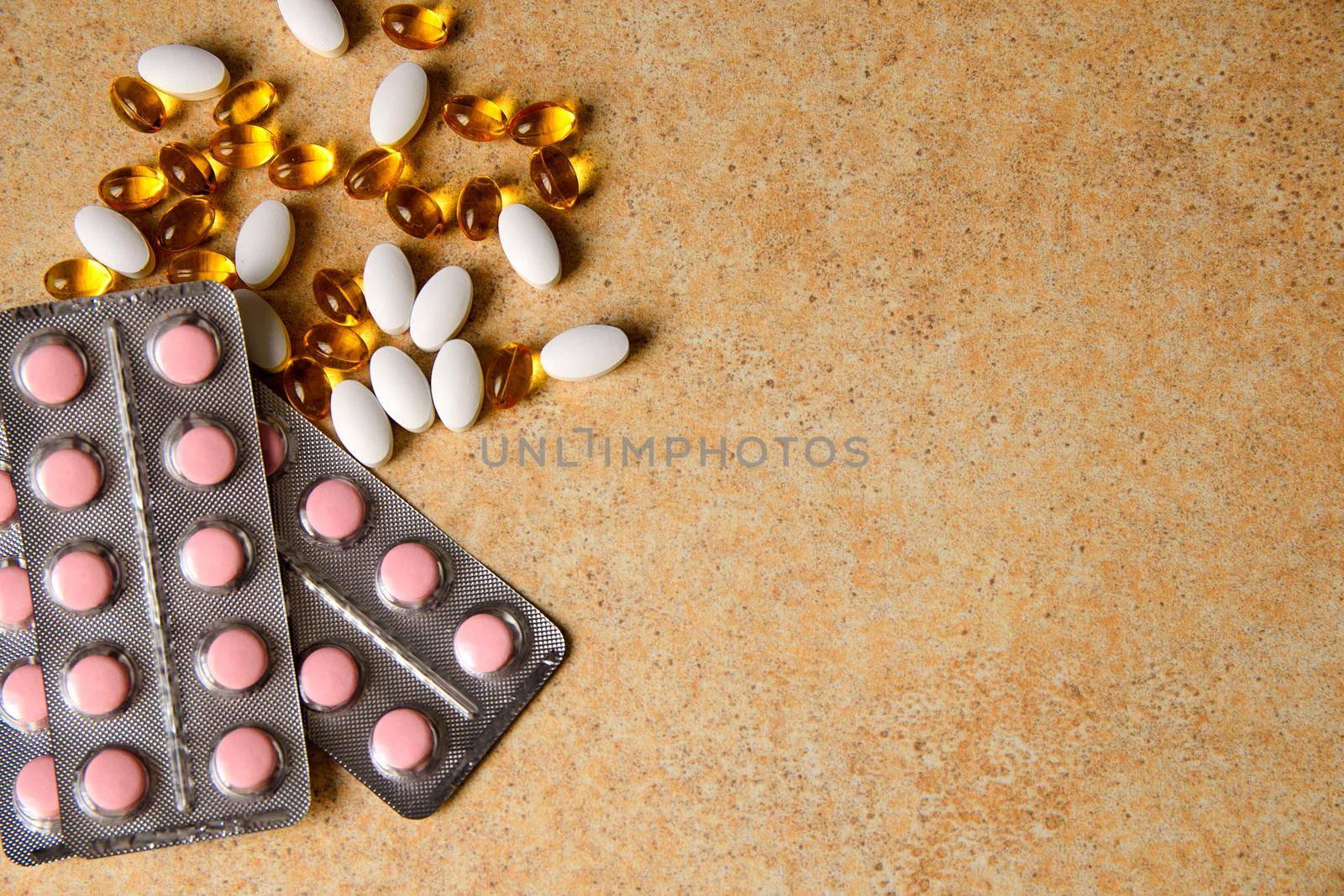 blister with pink tablets and vitamin D and capsules with fish oil lie chaotically against the background of a sand countertop