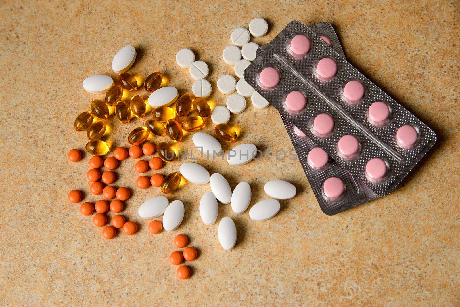 blister with pink and orange pills, vitamin D and fish oil capsules lie chaotically against a sandy tabletop