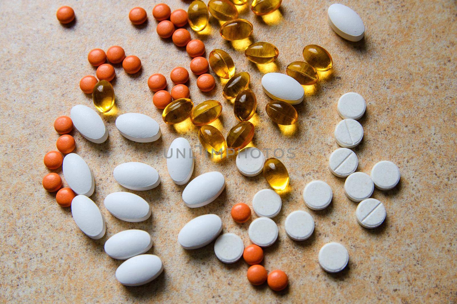 orange pills, vitamin D and fish oil capsules lie randomly against a sand countertop