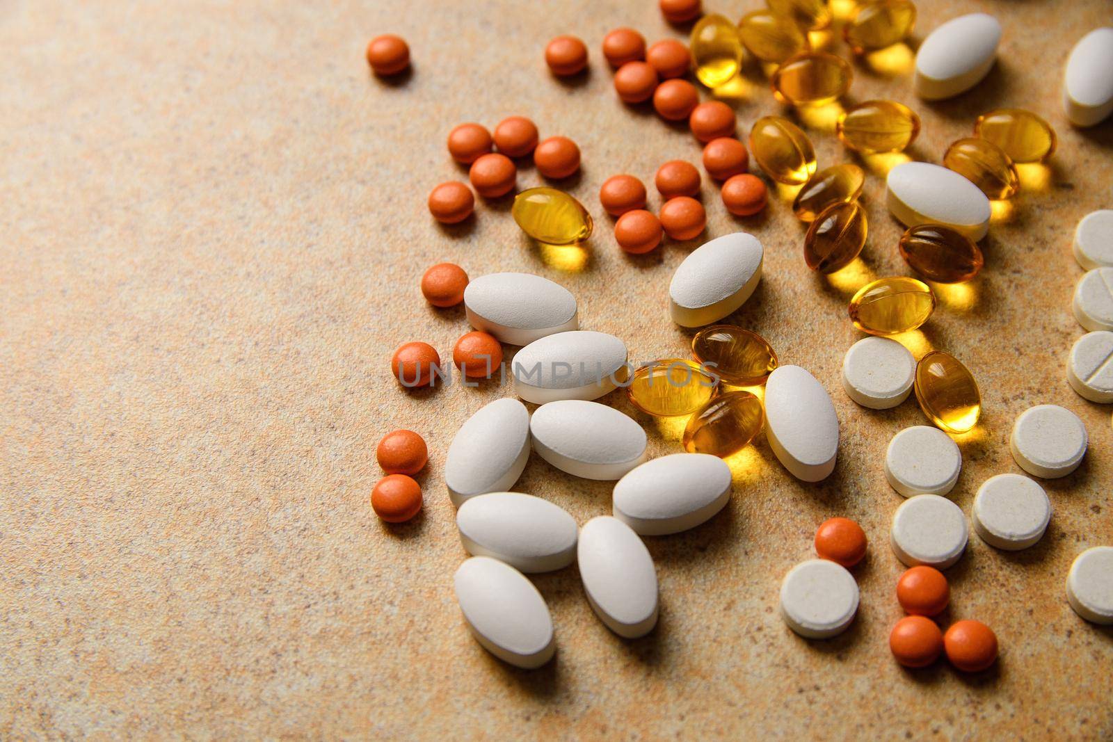 orange pills, vitamin D and fish oil capsules lie randomly against a sand countertop