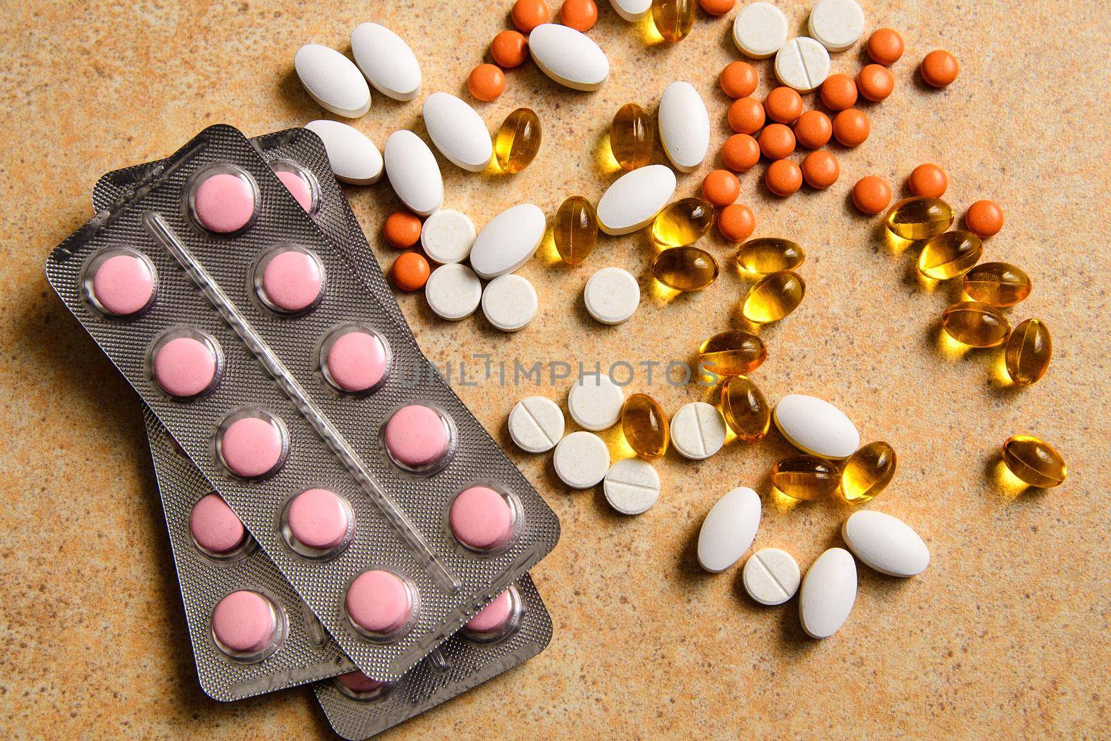 Blister with pink and orange pills, vitamin D and fish oil capsules randomly lie on sand background countertops