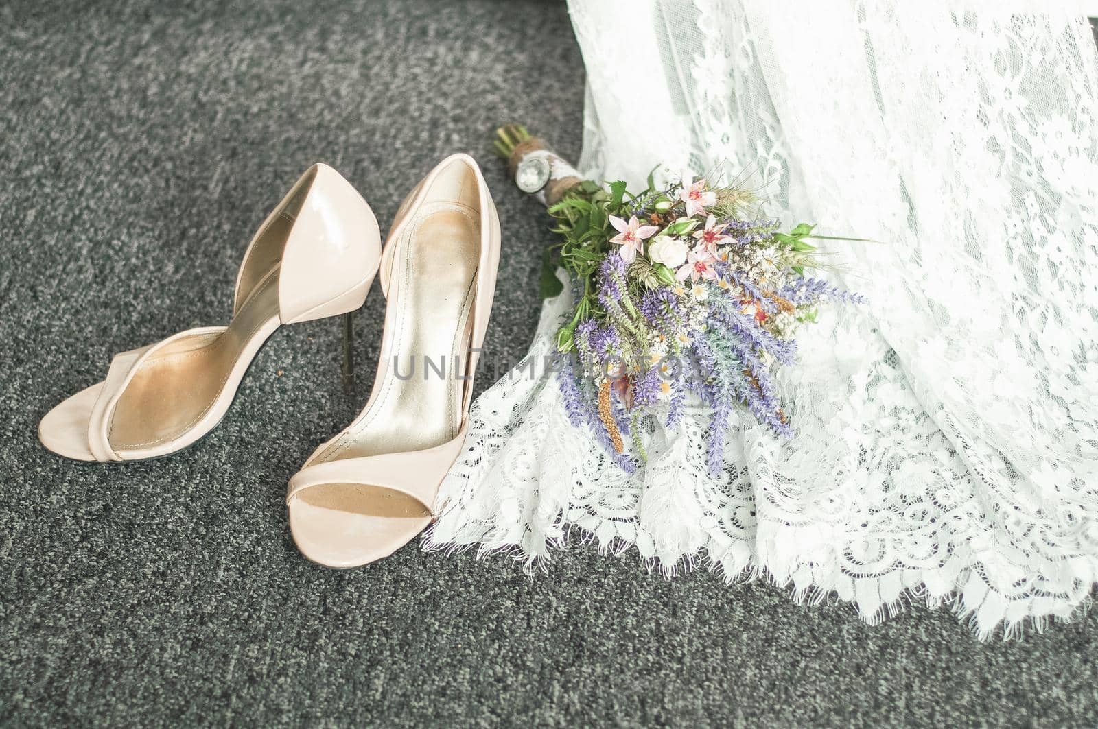 wedding shoes on the rug next to the bridal bouquet and dress