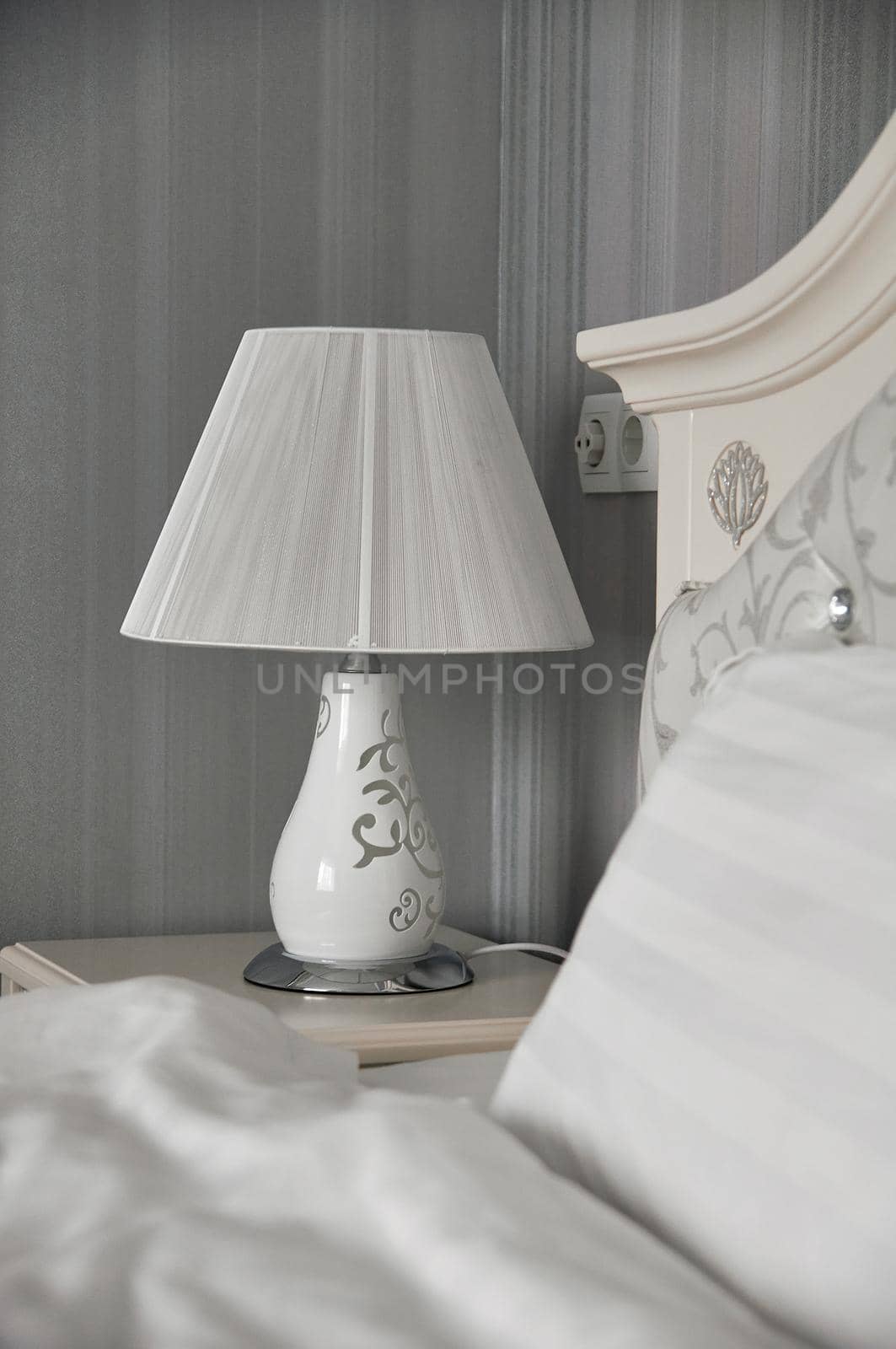 table lamp on a bedside table in a bedroom with gray walls near the bed is lit with yellow light