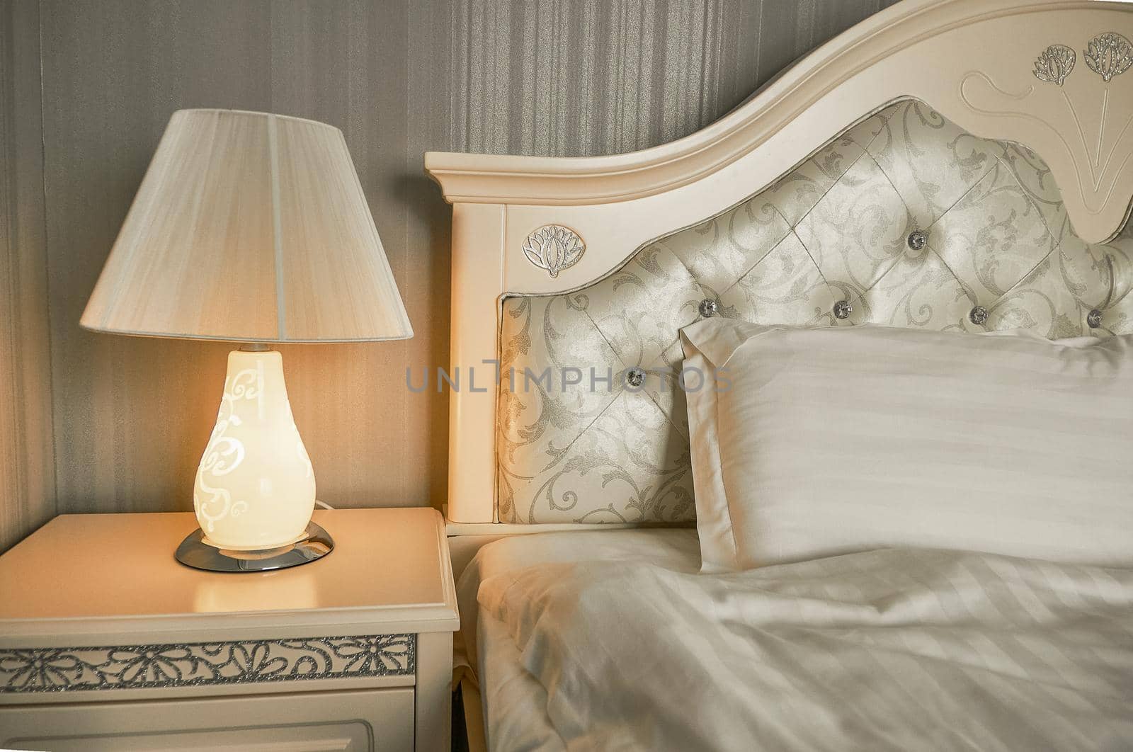 table lamp on a bedside table in a bedroom with gray walls near the bed is lit with yellow light